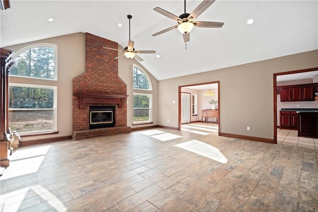 unfurnished living room featuring a wealth of natural light, light hardwood / wood-style flooring, high vaulted ceiling, and a brick fireplace