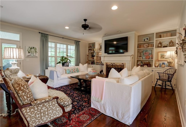 living room with built in shelves, dark hardwood / wood-style flooring, ornamental molding, and ceiling fan