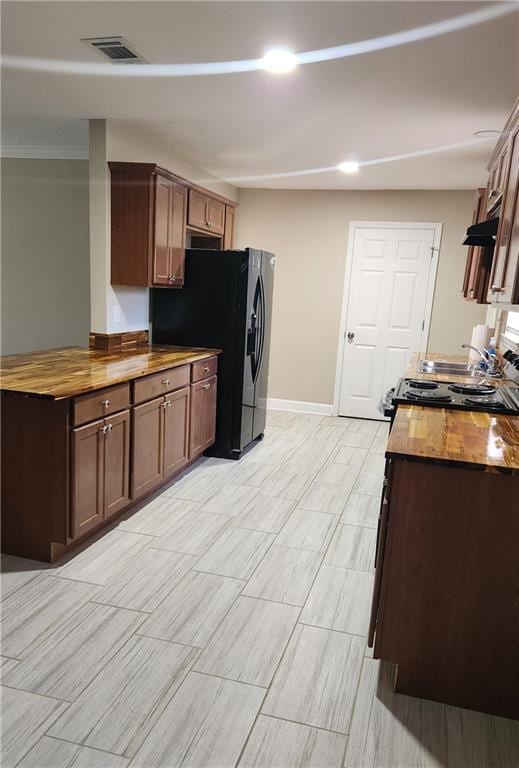 kitchen featuring stainless steel stove, butcher block countertops, and black refrigerator with ice dispenser