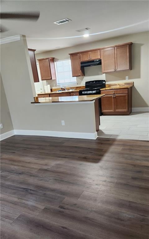 kitchen with kitchen peninsula, dark hardwood / wood-style floors, ornamental molding, and black range with gas cooktop