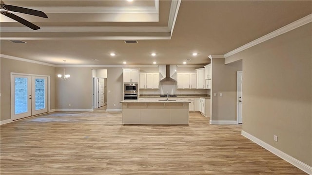 kitchen featuring white cabinetry, a center island with sink, wall chimney exhaust hood, and french doors