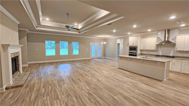 kitchen featuring white cabinetry, wall chimney range hood, light hardwood / wood-style floors, a tray ceiling, and appliances with stainless steel finishes