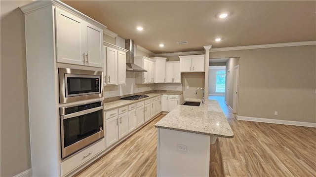 kitchen featuring sink, wall chimney range hood, a center island with sink, white cabinets, and appliances with stainless steel finishes