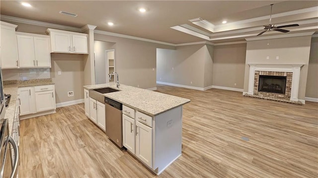 kitchen featuring white cabinets, sink, stainless steel dishwasher, a fireplace, and an island with sink