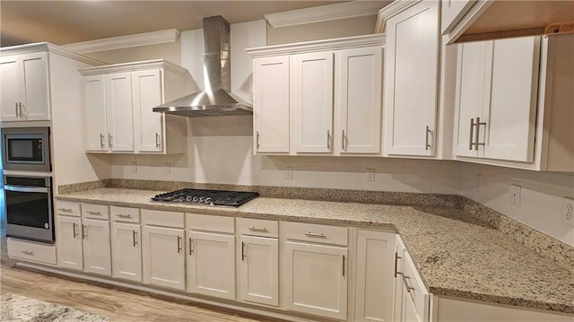 kitchen featuring white cabinets, ornamental molding, wall chimney range hood, and appliances with stainless steel finishes