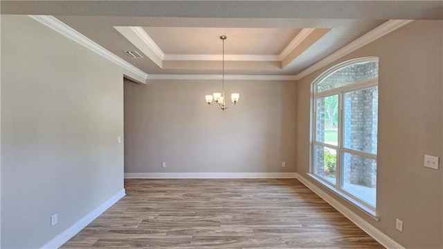 spare room with light hardwood / wood-style floors, a raised ceiling, crown molding, and an inviting chandelier