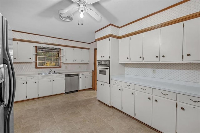 kitchen with a sink, white cabinets, light countertops, appliances with stainless steel finishes, and wallpapered walls