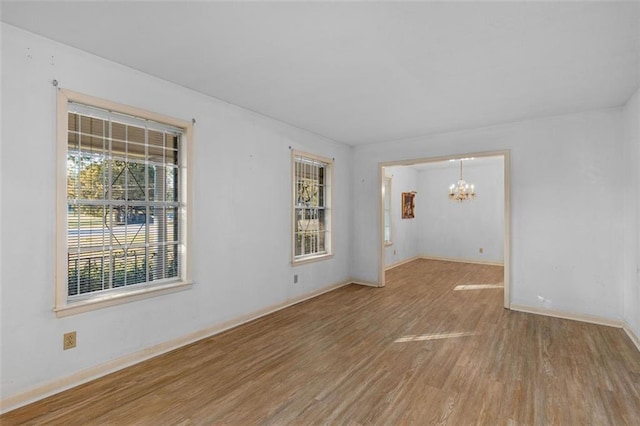 spare room featuring baseboards, an inviting chandelier, and wood finished floors