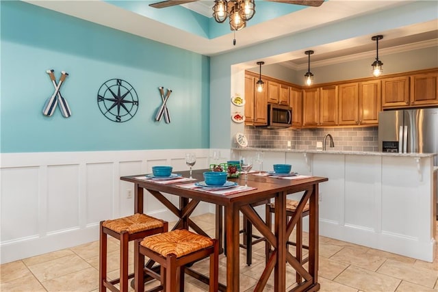 kitchen featuring backsplash, appliances with stainless steel finishes, brown cabinetry, a sink, and a peninsula