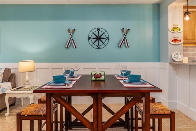 dining space with wainscoting, a decorative wall, and light tile patterned flooring