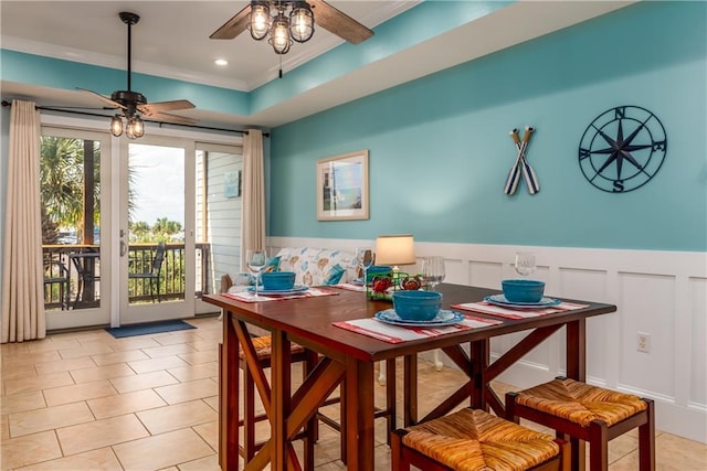 dining area with ceiling fan, light tile patterned flooring, a decorative wall, ornamental molding, and wainscoting