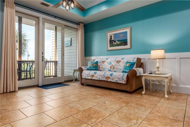 interior space with ceiling fan, a decorative wall, visible vents, wainscoting, and a tray ceiling