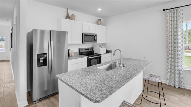 kitchen with appliances with stainless steel finishes, white cabinetry, sink, a kitchen island with sink, and light stone counters