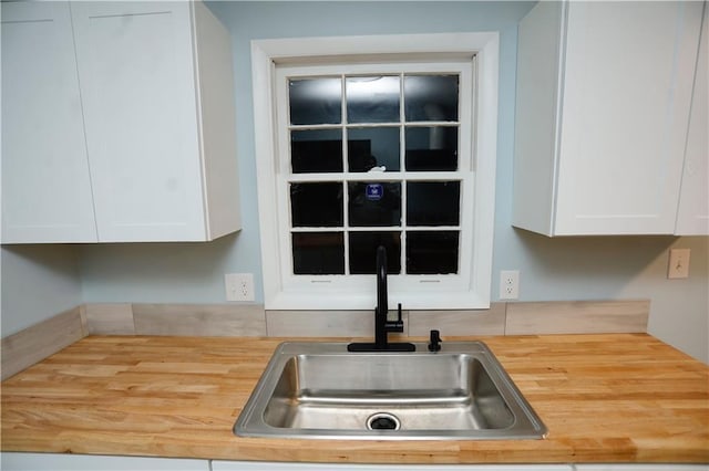 kitchen featuring white cabinets, wood counters, and a sink