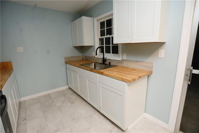 kitchen with butcher block counters, baseboards, white cabinetry, and a sink