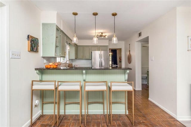 kitchen featuring a kitchen breakfast bar, kitchen peninsula, stainless steel refrigerator, and green cabinetry