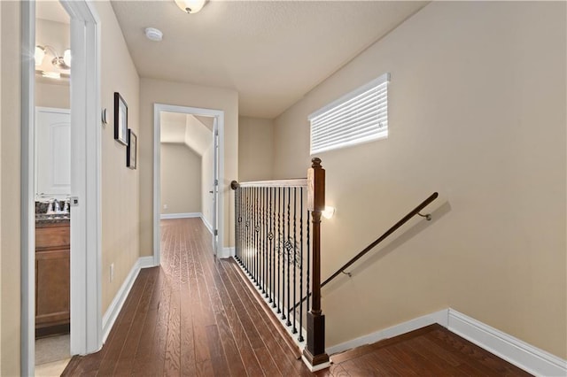 corridor featuring baseboards, dark wood finished floors, and an upstairs landing