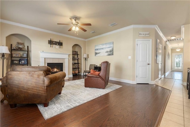 living room featuring visible vents, ornamental molding, wood finished floors, a tile fireplace, and baseboards