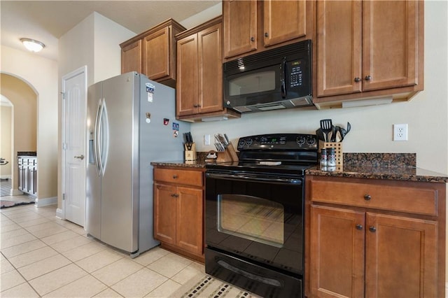 kitchen with black appliances, arched walkways, brown cabinets, and dark stone countertops