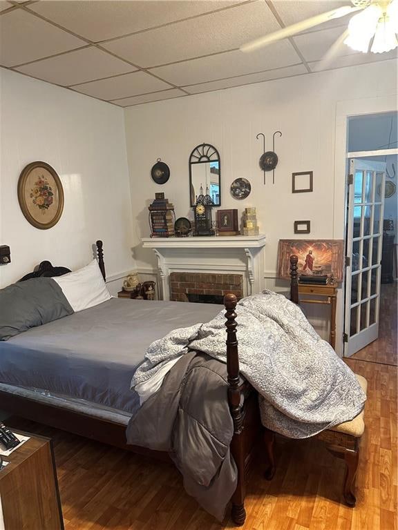 bedroom with ceiling fan, hardwood / wood-style flooring, a fireplace, and a drop ceiling