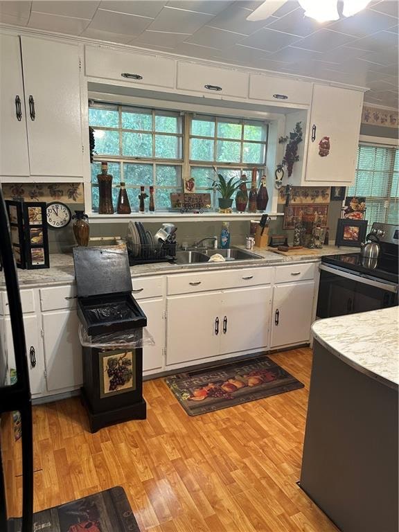 kitchen with white cabinets, sink, electric stove, and light hardwood / wood-style floors