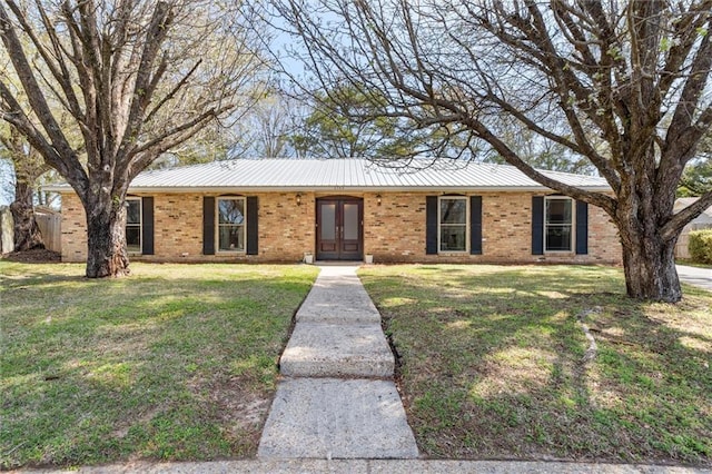 single story home featuring a front yard, brick siding, and metal roof