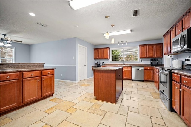 kitchen with decorative light fixtures, stainless steel appliances, ceiling fan, a kitchen island, and a textured ceiling