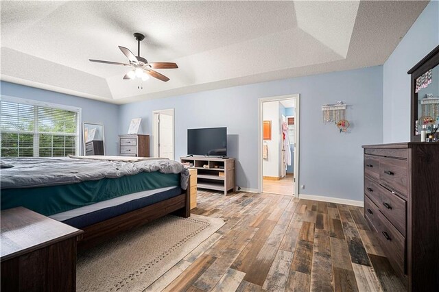 bedroom featuring a tray ceiling, dark hardwood / wood-style flooring, a textured ceiling, and ceiling fan