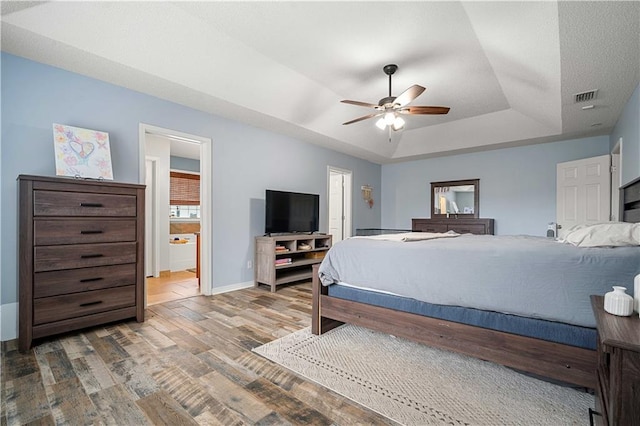 bedroom with a raised ceiling, ceiling fan, ensuite bathroom, and hardwood / wood-style flooring