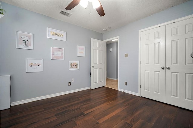 unfurnished bedroom featuring dark wood-type flooring, a closet, ceiling fan, and a textured ceiling