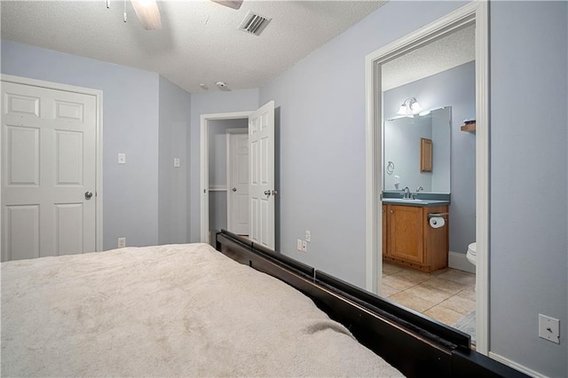 bedroom with a textured ceiling, light tile patterned floors, connected bathroom, sink, and ceiling fan