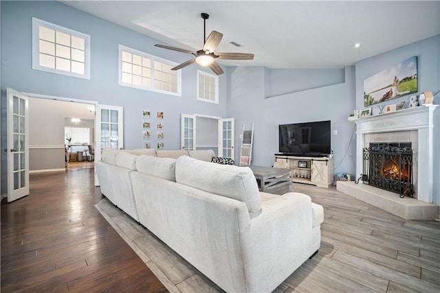 living room with high vaulted ceiling, a tile fireplace, ceiling fan, and light hardwood / wood-style floors