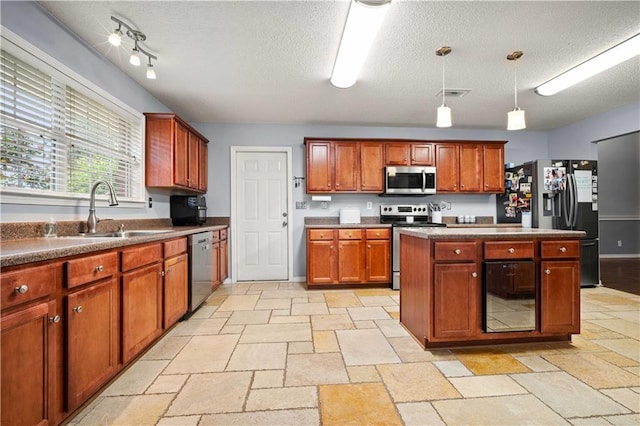 kitchen with a textured ceiling, stainless steel appliances, sink, and hanging light fixtures