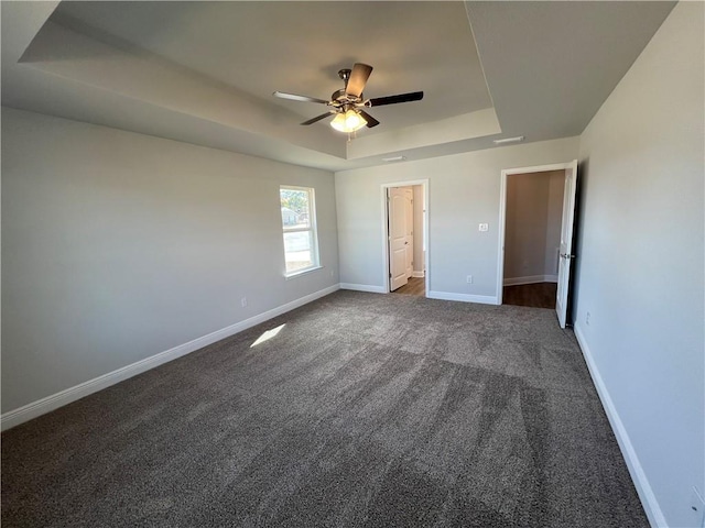 unfurnished bedroom with ceiling fan, a tray ceiling, and carpet flooring