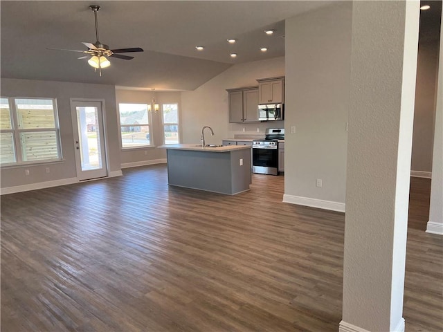 kitchen with ceiling fan, vaulted ceiling, appliances with stainless steel finishes, an island with sink, and dark hardwood / wood-style floors