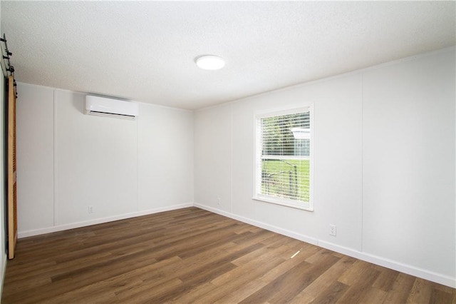 unfurnished room with a textured ceiling, a barn door, a wall unit AC, and wood finished floors