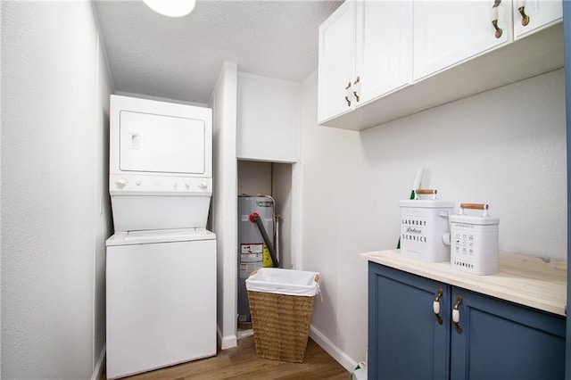 laundry room featuring stacked washer and dryer, cabinet space, baseboards, wood finished floors, and electric water heater