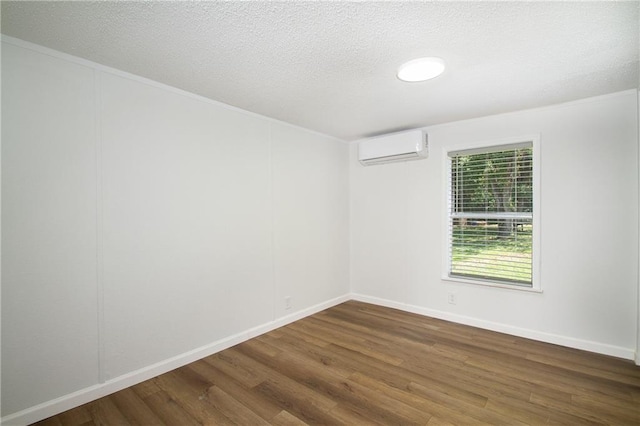 empty room with a textured ceiling, a wall unit AC, wood finished floors, and baseboards