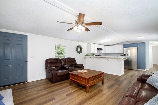 living area with vaulted ceiling with beams, a textured ceiling, wood finished floors, a ceiling fan, and baseboards