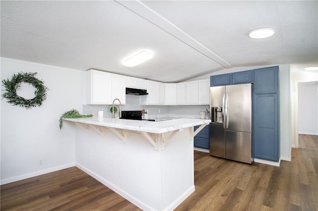 kitchen with a kitchen bar, a peninsula, stainless steel fridge, under cabinet range hood, and black / electric stove