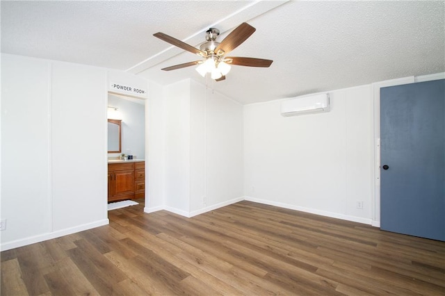 unfurnished bedroom with a textured ceiling, wood finished floors, vaulted ceiling, an AC wall unit, and ensuite bath