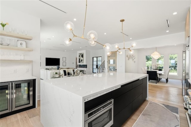 kitchen with hanging light fixtures, stainless steel range, a large island, oven, and light hardwood / wood-style floors