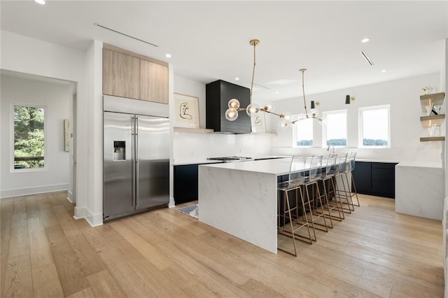 kitchen with a kitchen island, a kitchen breakfast bar, built in refrigerator, hanging light fixtures, and light hardwood / wood-style flooring