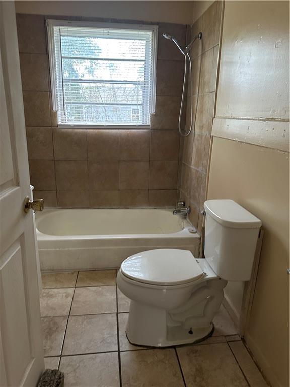 bathroom featuring toilet, tiled shower / bath combo, and tile patterned flooring