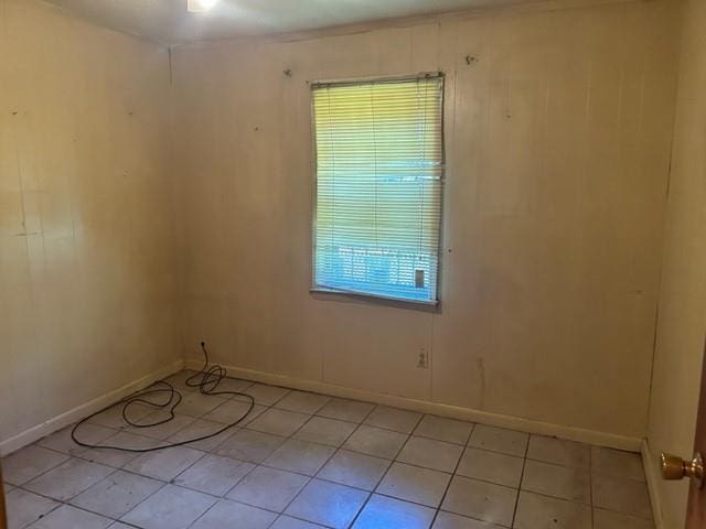 empty room with light tile patterned floors, baseboards, and wood walls