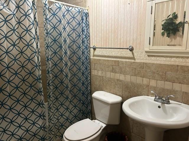 bathroom with toilet, tile walls, a shower with curtain, and a sink