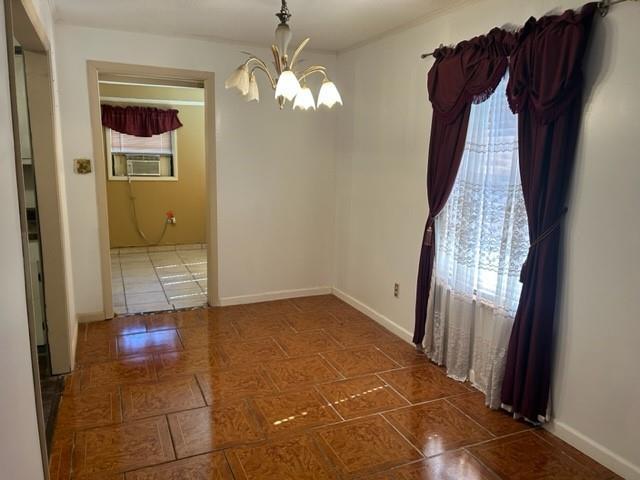 spare room featuring a notable chandelier, cooling unit, baseboards, and a wealth of natural light