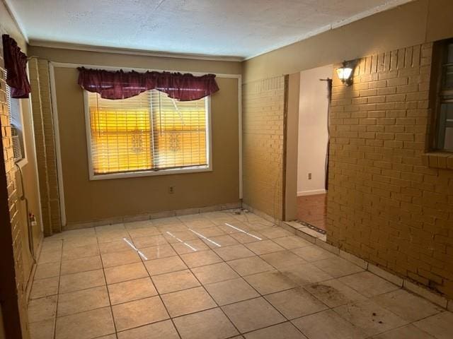 unfurnished room with light tile patterned flooring, brick wall, and a textured ceiling