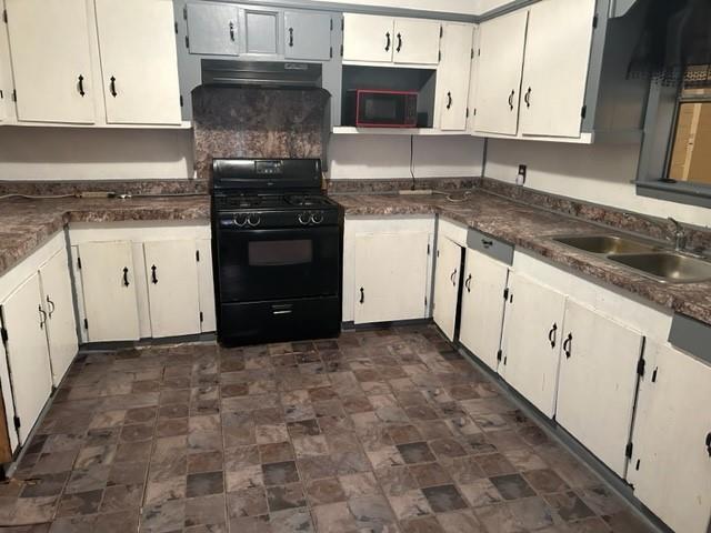 kitchen with dark countertops, under cabinet range hood, black gas range, white cabinetry, and a sink