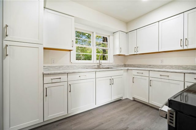 kitchen with electric range, sink, white cabinets, and light hardwood / wood-style floors